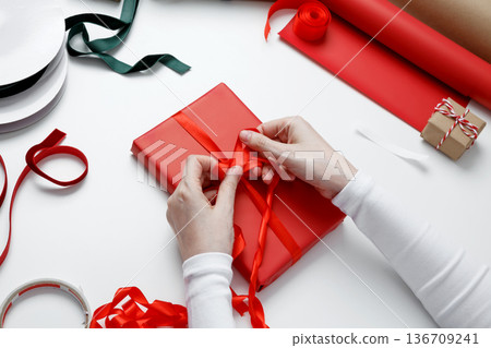 Woman tying decorative bow on paper wrapped gift during celebration preparation Woman tying decorative bow on paper wrapped gift during celebration preparation 136709241