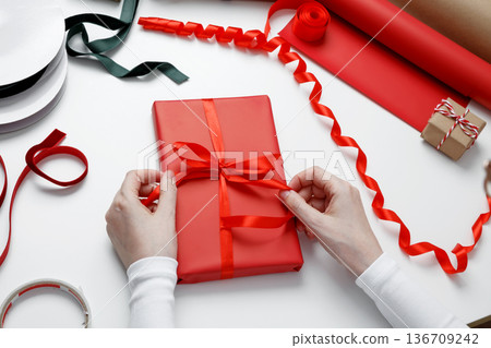 Woman tying decorative bow on paper wrapped gift during celebration preparation Woman tying decorative bow on paper wrapped gift during celebration preparation 136709242