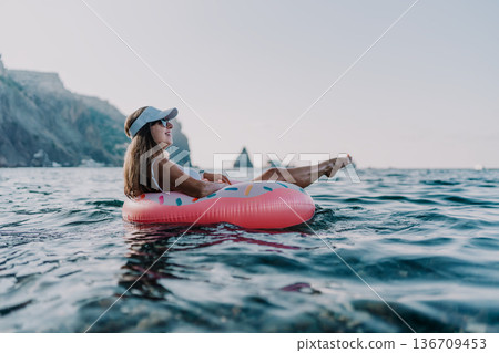 Woman, float, ocean. Young woman relaxing on a donut inflatable in the sea with scenic cliffs. Woman, float, ocean. Young woman relaxing on a donut inflatable in the sea with scenic cliffs. 136709453