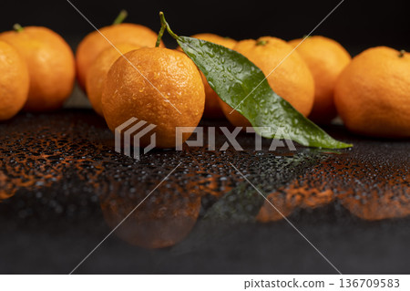 wet fresh orange small tangerines with leaves are reflected on a black mirror , a group of ripe sweet tangerines with green leaves covered with drops of clear water with reflection on a black glass wet fresh orange small tangerines with leaves are reflected on a black mirror , a group of ripe sweet tangerines with green leaves covered with drops of clear water with reflection on a black glass 136709583