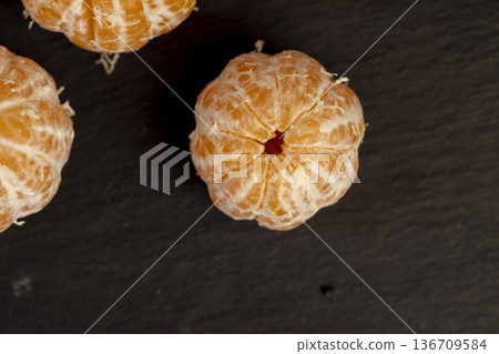 a juicy orange-colored peeled tangerine on a black slate table, a ripe orange small mandarin without a peel on a black slate board a juicy orange-colored peeled tangerine on a black slate table, a ripe orange small mandarin without a peel on a black slate board 136709584