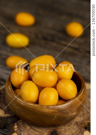 small orange fruits of juicy fresh and fragrant kumquat on a black wooden table, oval oblong kumquat fruit on a black table made of pine wood small orange fruits of juicy fresh and fragrant kumquat on a black wooden table, oval oblong kumquat fruit on a black table made of pine wood 136709590