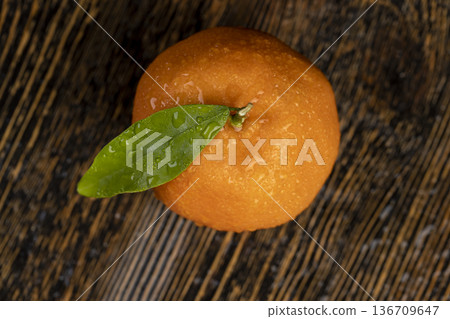wet juicy ripe tangerine with one green leaf, fruit on a wooden table, unpeeled ripe with orange peel, a small tangerine with a long green leaf covered with drops of water wet juicy ripe tangerine with one green leaf, fruit on a wooden table, unpeeled ripe with orange peel, a small tangerine with a long green leaf covered with drops of water 136709647