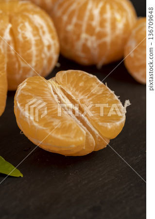 sliced juicy peeled orange tangerine on a black slate table, ripe orange mandarin without peel on a black slate board, tangerine divided into small slices sliced juicy peeled orange tangerine on a black slate table, ripe orange mandarin without peel on a black slate board, tangerine divided into small slices 136709648