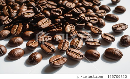 Roasted brown coffee beans are scattered casually across a clean white surface, showing their textured details and inviting aroma for a morning brew experience. 136709830