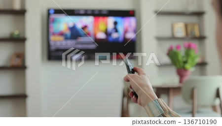 Woman selects tv channels with remote control at living room on sofa. Woman selects tv channels with remote control at living room on sofa. 136710190