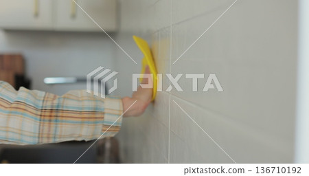 Woman cleaning the kitchen wall. Cleaning, hands and spray bottle with person in kitchen of home for chores, housework or hygiene. 136710192