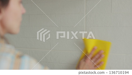Woman cleaning the kitchen wall. Cleaning, hands and spray bottle with person in kitchen of home for chores, housework or hygiene. 136710194