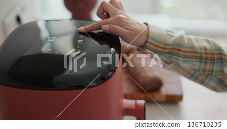 Woman at home using trendy kitchen gadget, deep fryer, selecting program. 136710235