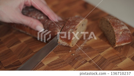 Closeup woman hand cutting bread on wooden board. Homemade healthy cooking concept. Closeup woman hand cutting bread on wooden board. Homemade healthy cooking concept. 136710237