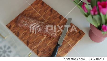 Woman slices bread on wooden cutting board in modern kitchen. Woman slices bread on wooden cutting board in modern kitchen. 136710241