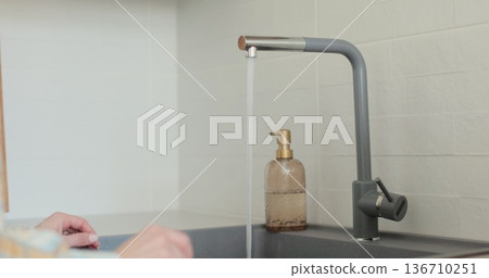 Woman turns on the tap in a modern white kitchen. Modern kitchen room in minimalist apartment. 136710251