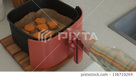 Woman cooking tasty chicken nuggets in air fryer. Healthy food for diet eating. 136710264