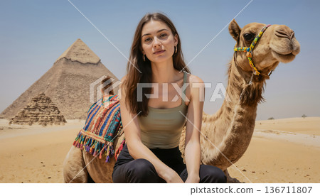 A young woman sits and poses for the camera against the backdrop of the Great Pyramids and the sky. A young woman sits and poses for the camera against the backdrop of the Great Pyramids and the sky. 136711807