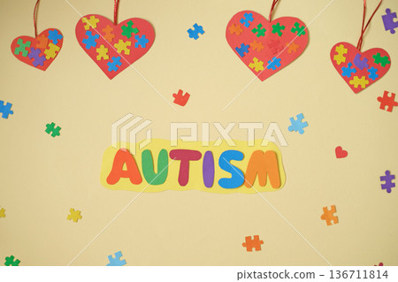 The inscription autism on a yellow background decorated with multicolored puzzle pieces and hearts suspended on a ribbon. Autism Awareness The inscription autism on a yellow background decorated with multicolored puzzle pieces and hearts suspended on a ribbon. Autism Awareness 136711814