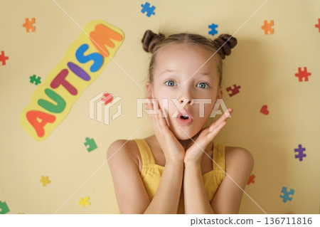 Portrait of surprised young girl with colorful Autism sign and puzzle pieces on yellow background. Concept of autism awareness, neurodiversity acceptance, inclusive education and child support Portrait of surprised young girl with colorful Autism sign and puzzle pieces on yellow background. Concept of autism awareness, neurodiversity acceptance, inclusive education and child support 136711816