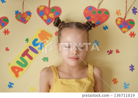 A beautiful peaceful girl with her eyes closed in the process of thinking on a background decorated with puzzles and hearts. The complexity and variety of manifestations of Autism. A beautiful peaceful girl with her eyes closed in the process of thinking on a background decorated with puzzles and hearts. The complexity and variety of manifestations of Autism. 136711819
