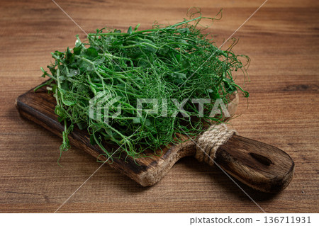 Freshly harvested pea shoots displayed on a rustic wooden cutting board against a textured wooden backdrop Freshly harvested pea shoots displayed on a rustic wooden cutting board against a textured wooden backdrop 136711931