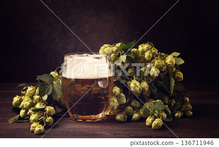 A mug of beer , on a wooden table, with a branch of fresh hops, rustic , no people, 136711946