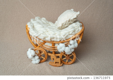 Small handmade rattan pram with soft white bedding. Styled newborn photography prop in neutral beige tones. Perfect for baby studio sessions and minimal lifestyle concepts. 136711973