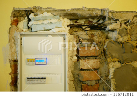 Electrical distribution panel board circuit breaker consumer close-up unit fuse box controlling power feed attached in red brick and mortal wall cement thick layers mortal or plaster in renovation or Electrical distribution panel board circuit breaker consumer close-up unit fuse box controlling power feed attached in red brick and mortal wall cement thick layers mortal or plaster in renovation or 136712011