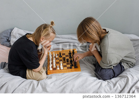 Clever little girl and young boy have a nice game. Sibling playing chess on the bed at home together 136712364