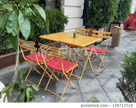 Outdoor seating area at a cafe with yellow tables and chairs surrounded by green plants in the city Outdoor seating area at a cafe with yellow tables and chairs surrounded by green plants in the city 136712528