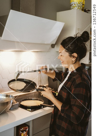 Woman Smiling While Cooking Pancakes in Kitchen 136712549