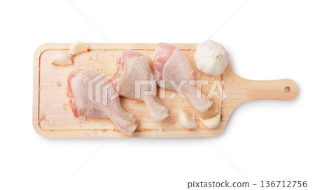 Top view of three raw chicken drumsticks on a wooden board with garlic and salt, isolated on a white background. Fresh poultry meat ready for cooking. High quality photo 136712756