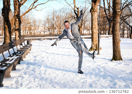 Man losing balance and slipping on an icy path in a snowy park. Winter accident concept showing the risk of falling, slippery footwear, and injury danger outdoors. High quality photo Man losing balance and slipping on an icy path in a snowy park. Winter accident concept showing the risk of falling, slippery footwear, and injury danger outdoors. High quality photo 136712762