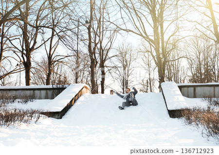 Man slipping and falling down icy stairs in a winter park. Dangerous slippery steps covered with ice and snow. Concept of winter accident, injury risk, cold weather hazard and personal safety. Man slipping and falling down icy stairs in a winter park. Dangerous slippery steps covered with ice and snow. Concept of winter accident, injury risk, cold weather hazard and personal safety. 136712923