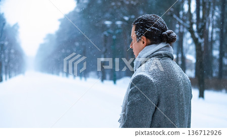A lone man in a grey coat stands in a snowy park, gazing into the distance; a poignant image evoking deep depression, solitude, and the quiet journey of a lonely soul. High quality photo 136712926