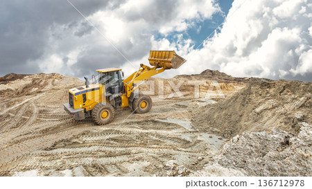 A large yellow loader moves earth and gravel at a construction site during the day, while clouds form in the sky. Heavy equipment leveling the construction site A large yellow loader moves earth and gravel at a construction site during the day, while clouds form in the sky. Heavy equipment leveling the construction site 136712978
