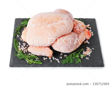 Whole frozen chicken carcass covered in ice crystals on a black slate board with dill and pink salt, isolated on white background. High quality photo 136712985