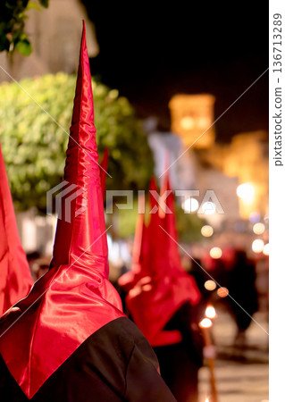 Many nazarenos with red hoods walking in procession Many nazarenos with red hoods walking in procession 136713289