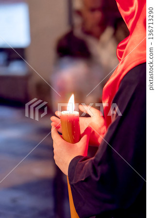 Detailed view of a hand holding a large lit candle in a religious procession 136713290