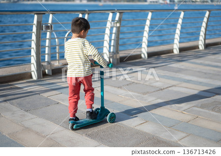 Child Enjoying The Outdoors On A Scooter By The Water Edge Child Enjoying The Outdoors On A Scooter By The Water Edge 136713426