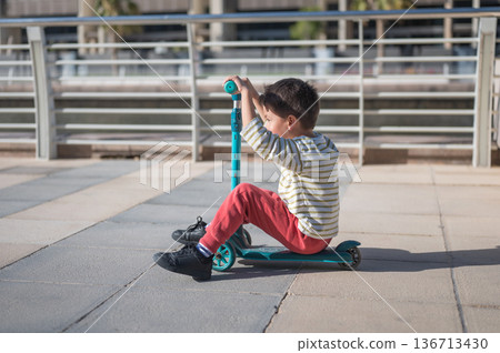 Child Enjoying Playtime On A Scooter In A Sunny Outdoor Setting 136713430