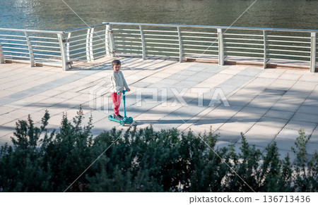 Young Boy Riding A Scooter In A Sunny Abu Dhabi Park Area 136713436