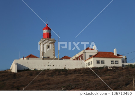 Red lighthouse tower and traditional white buildings at Cabo da Roca, Portugal. 136713490