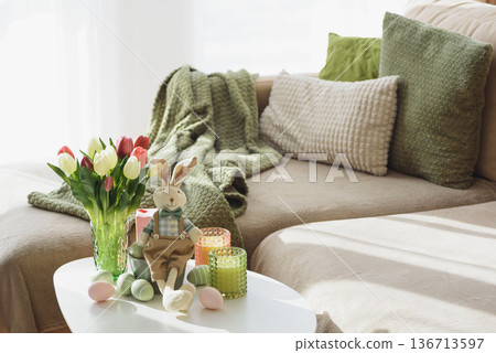 Living Room Decorated Easter Eggs with Bunny Figurines, Candles and Tulips. Cozy Spring Holiday Arrangement Living Room Decorated Easter Eggs with Bunny Figurines, Candles and Tulips. Cozy Spring Holiday Arrangement 136713597