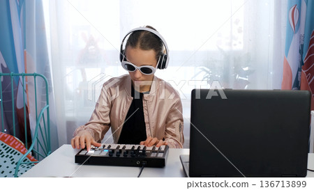 Girl in headphones and sunglasses makes music on midi keyboard, showing her fun and creative hobby at home Girl in headphones and sunglasses makes music on midi keyboard, showing her fun and creative hobby at home 136713899