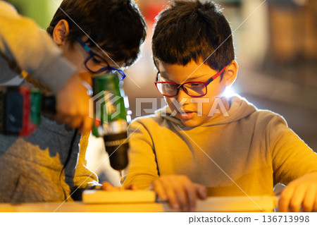 Young boys learning carpentry skills using a power drill 136713998