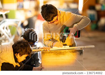 Kids learning woodworking using power drill in workshop 136714002