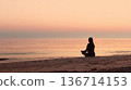 Woman Meditating On Beach At Sunrise, Silhouette Sitting In Lotus Pose By Calm Sea 136714153