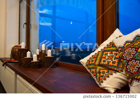 Cosy windowsill with candles and embroidered pillows at dusk 136715002