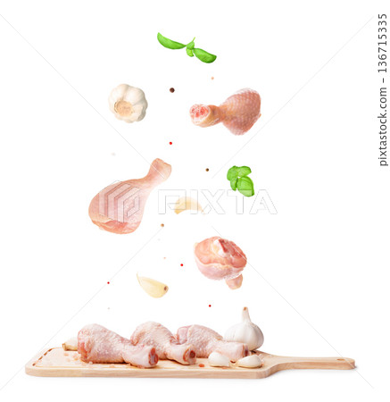 Flying raw chicken drumsticks with floating garlic, basil, and spices falling onto a wooden board isolated on a white background. High quality photo Flying raw chicken drumsticks with floating garlic, basil, and spices falling onto a wooden board isolated on a white background. High quality photo 136715335