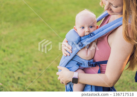 Mother using ergonomic baby carrier during a walk with her infant outdoors. Comfortable babywearing, active motherhood lifestyle, bonding, modern parenting, hands free care and everyday family routine Mother using ergonomic baby carrier during a walk with her infant outdoors. Comfortable babywearing, active motherhood lifestyle, bonding, modern parenting, hands free care and everyday family routine 136717518