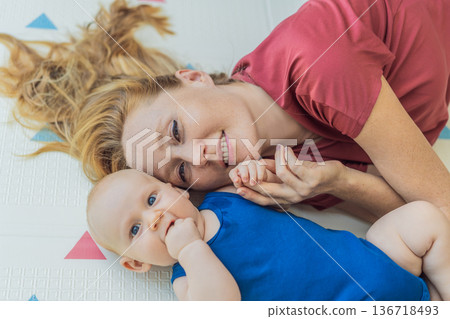 Mother and baby lying on a soft play mat at home, playing, talking and sharing a joyful moment together. Authentic family lifestyle, early childhood development and emotional bonding. Parenting and Mother and baby lying on a soft play mat at home, playing, talking and sharing a joyful moment together. Authentic family lifestyle, early childhood development and emotional bonding. Parenting and 136718493