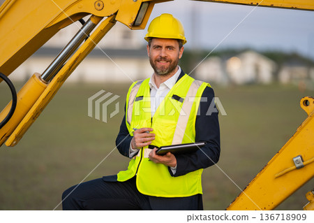 Civil engineer worker at a construction site. Engineer man in front of house background. Confident engineer worker at modern home building construction. Hispanic civil engineer in helmet. 136718909